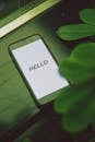 Close-up of a smartphone with 'Hello' text placed on a leafy green surface, emphasizing technology and nature.